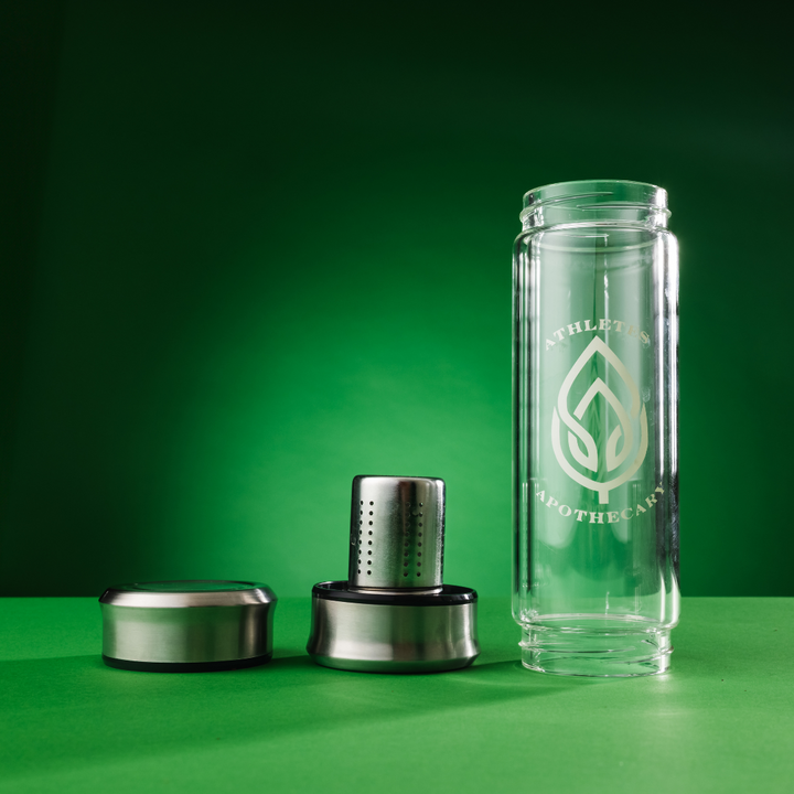 Glass tea infusing bottle, disassembled with a green background