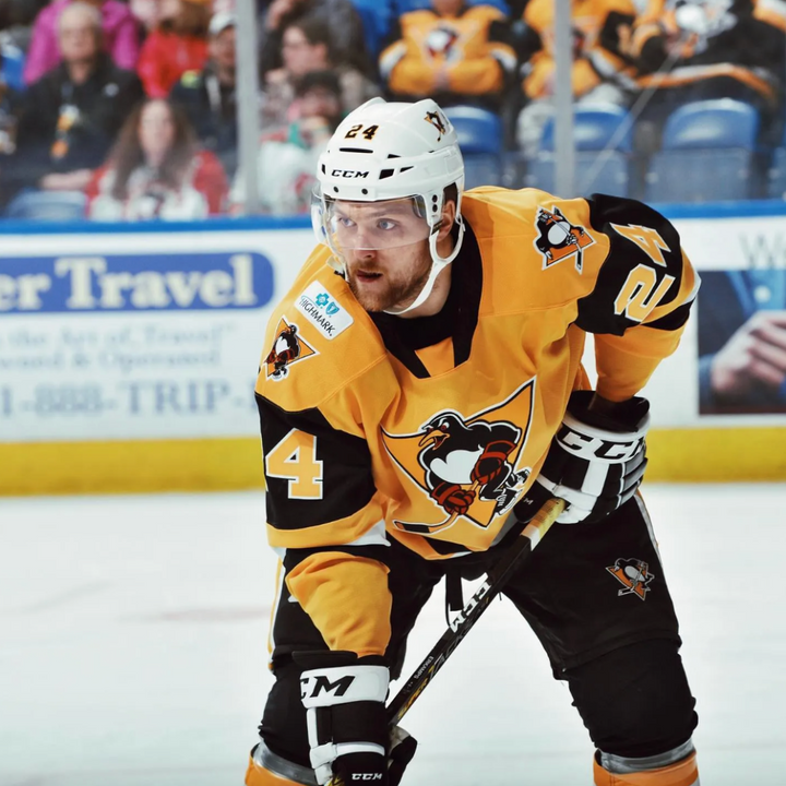 Hockey player in a yellow and black uniform on an ice rink with spectators in the background.