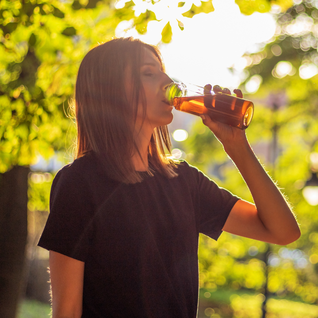 Athlete drinking tea in a park with the sun the background