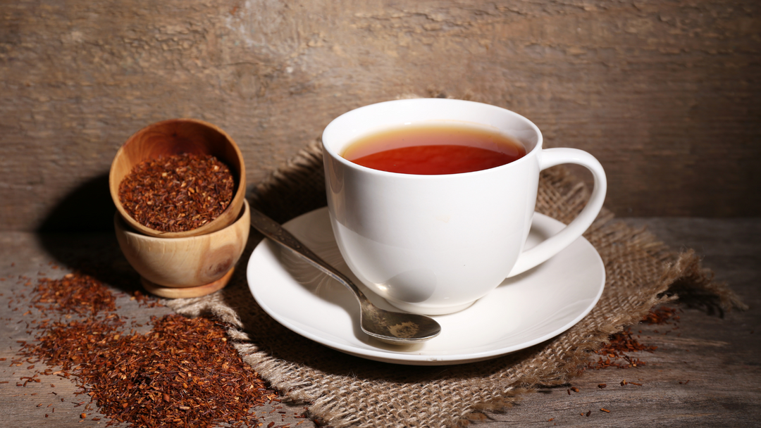 Rooibos tea freshly prepared in a mug with loose leaf around it. 