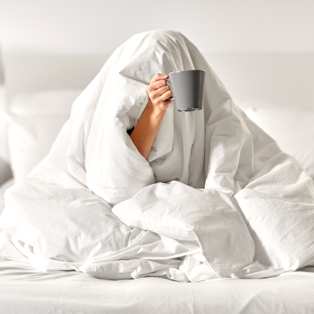 Person covered in blankets with a cup of tea in hand