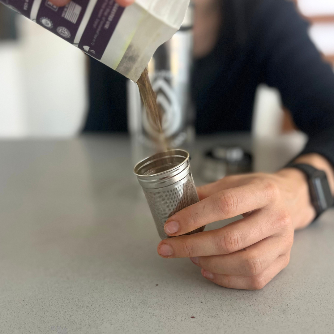 A portable, glass tea infuser bottle being filled with loose leaf tea